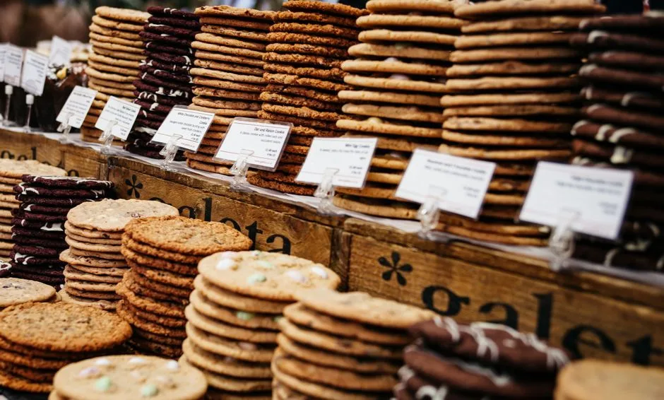 Assorted cookies elegantly stacked and labeled at a bustling market stall.