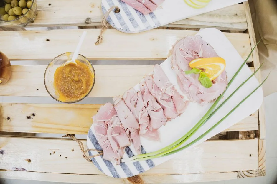 Fresh slices of ham with an orange garnish, served on a rustic board.