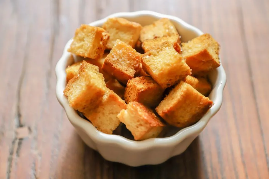 Close-up of golden-brown croutons in a white ceramic bowl on a rustic wooden table.