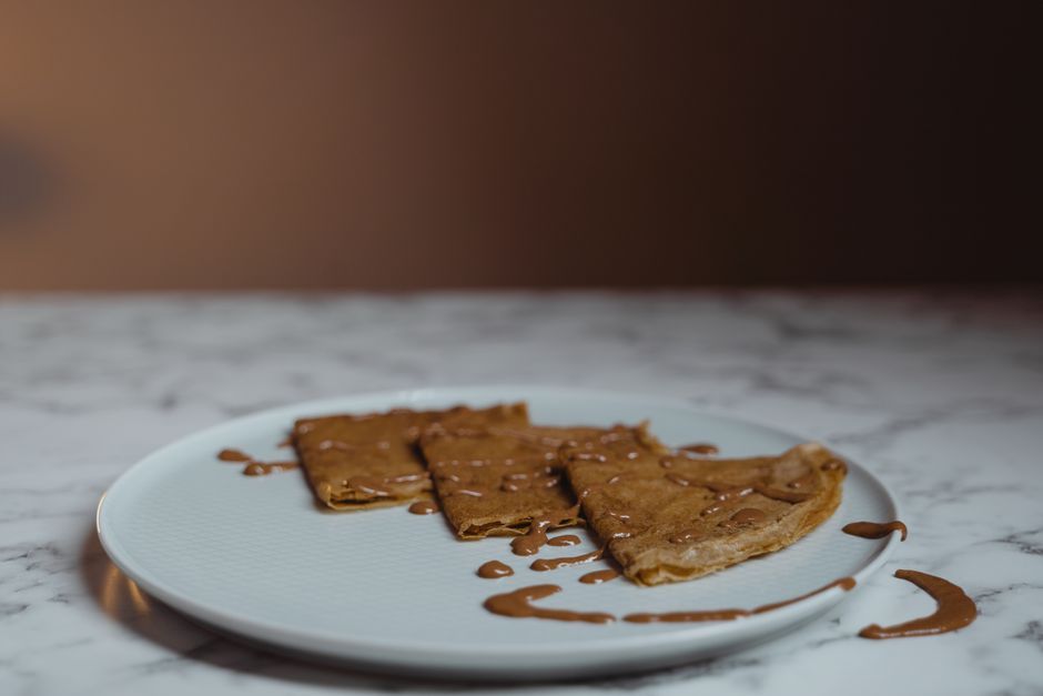 Savor the delightful taste of crepes drizzled with peanut butter on a ceramic plate.