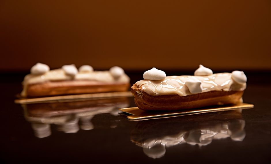 Delicious eclairs with white icing and meringue on golden trays, stylishly presented.